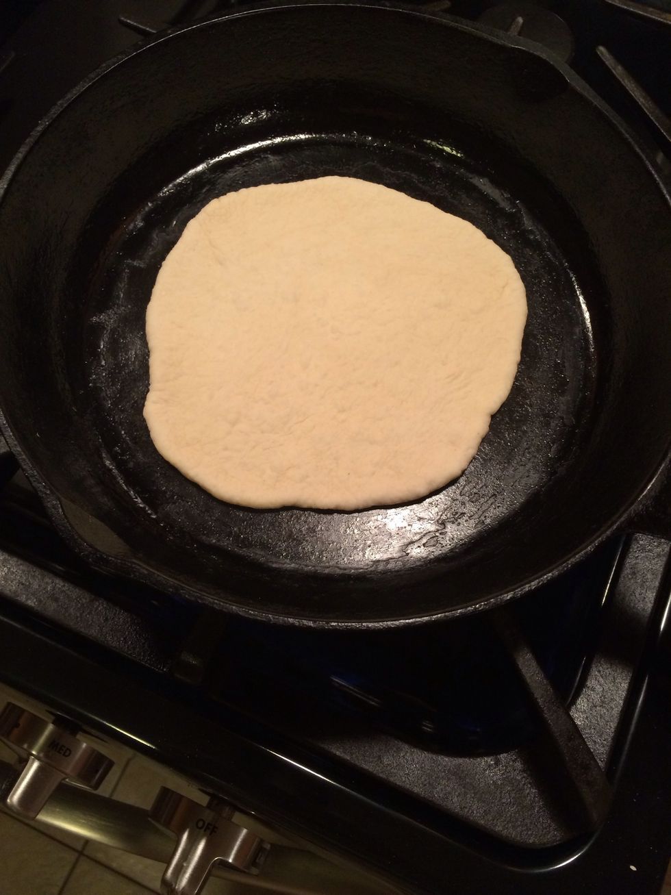Take your rolled out piece of pita dough and put it on the hot cast iron pan.