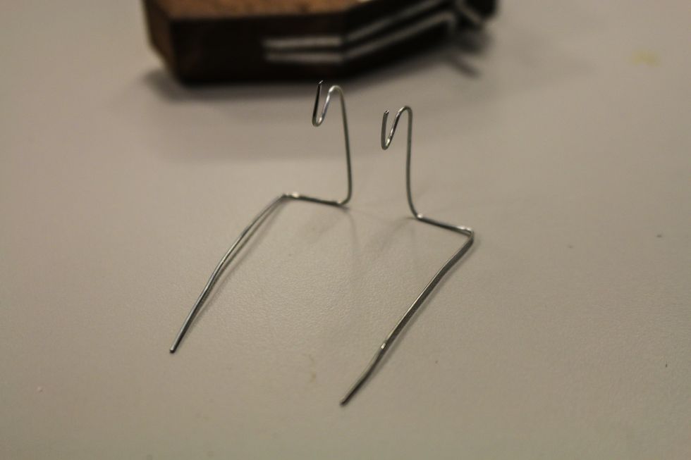 Taking off the second wire, sharpen the corners of the bends. You should be able to set them both down without tipping over. You can see where the hooks will hold the copper coil.