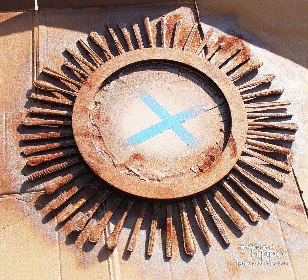 Tape off the center of the mirror to prep for painting. I wove wire around four of the knives to make a \u201cX\u201d across the back of the frame to create hanger.