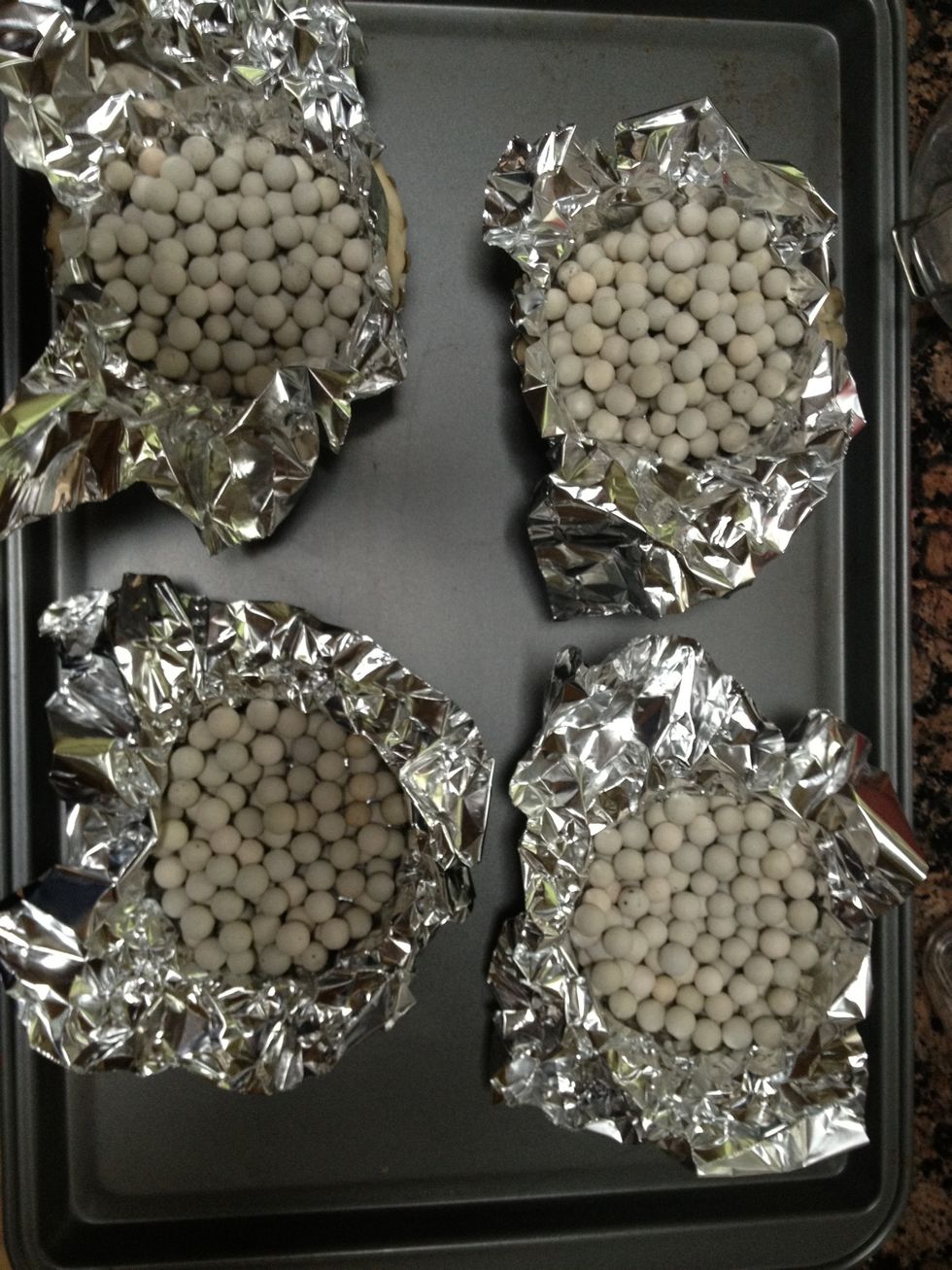 Tart shells must be "blind baked". Place a small piece of tinfoil into the raw dough and fill with pie weights or dry beans. Bake at 350 degrees Fahrenheit for 20 to 25 min.