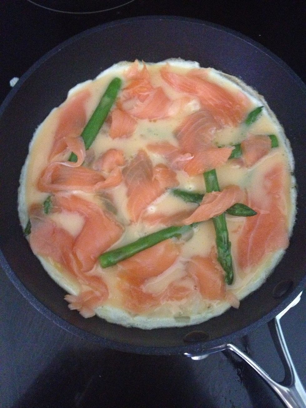 Tear of strips of the smoked salmon and throw them onto the cooking frittata. It doesn't need to be neat. Leave the frittata to cook like this for one or two minutes. Don't let it burn underneath.