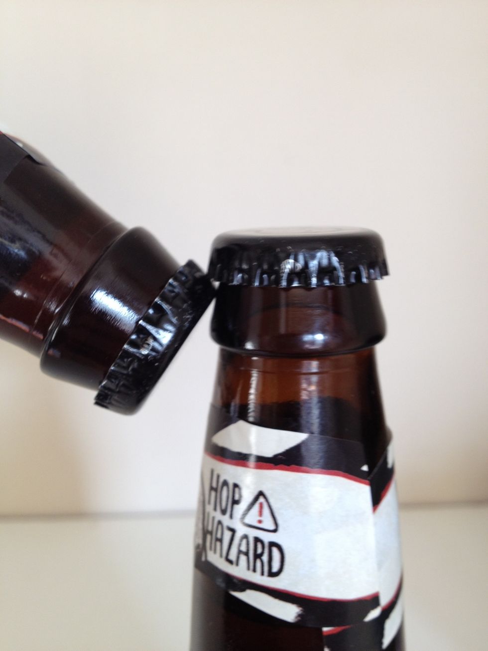 The beer you don't want to open (#2) will pop off the cap to your beer. Place smooth part of #2 cap under the cap of #1.
