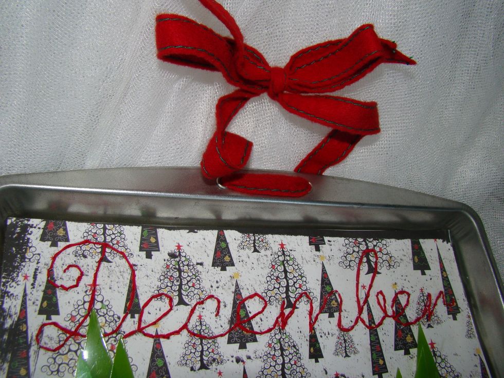 The final step, I took a crop a dial and punched two holes in the top of the cookie sheet, then ran ribbon through it to hang on wall.