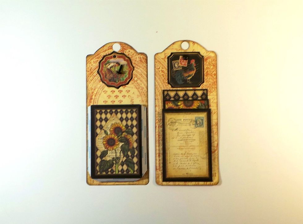 The first tags each get one of the pockets made in Step 41. Two long photo mats (Step 45) go in each pocket. Use the tags to create space in the pocket. Add a brad to the chipboard tag and adhere.