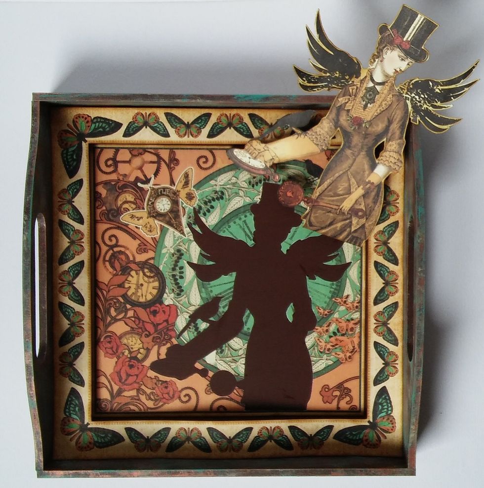 The frame has already been glued down in Step 1. You can now adhere the butterfly border. After adding the chipboard gears and embellishments. you can adhere the steampunk lady with adhesive foam.