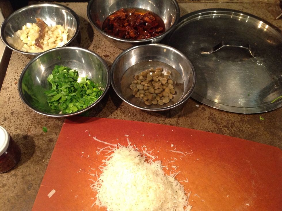 The ingredients for dressing the pasta: anchovy and garlic, capers (soaking as they were packed in salt), sundried tomatoes, parsley and cheese. Start heating the oil once the pasta water is boiling.