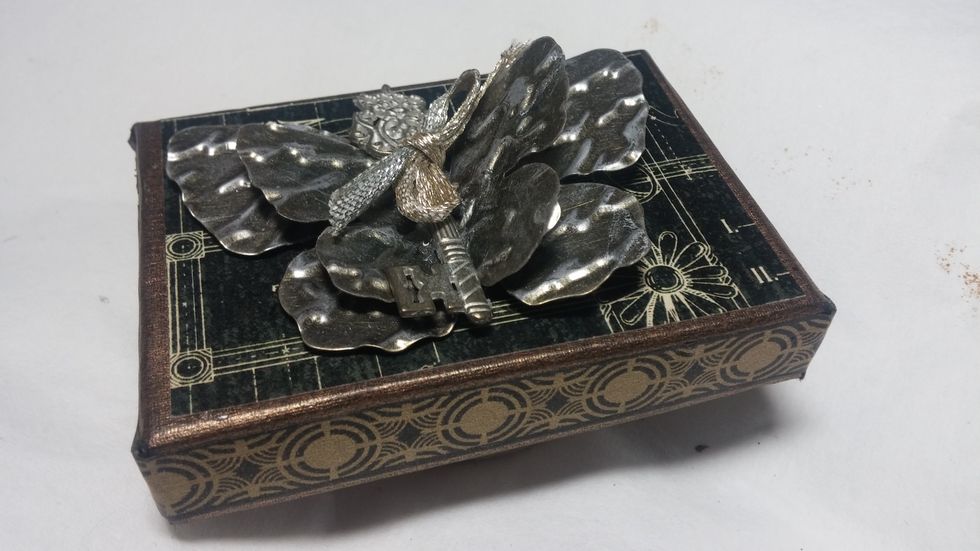 The inside focal was created on a jewelry box top. Layers of embossed butterflies are finished off with a Graphic 45 key and a ribbon. All glued on to add to the inside of the box.