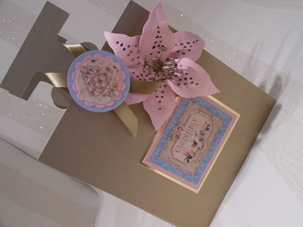 The perfume bottle album has greyboard covers that were covered in gold card. A cutapart was used as the label for the perfume bottle. Layered motif used at the neck. Flower die cut and hand embossed
