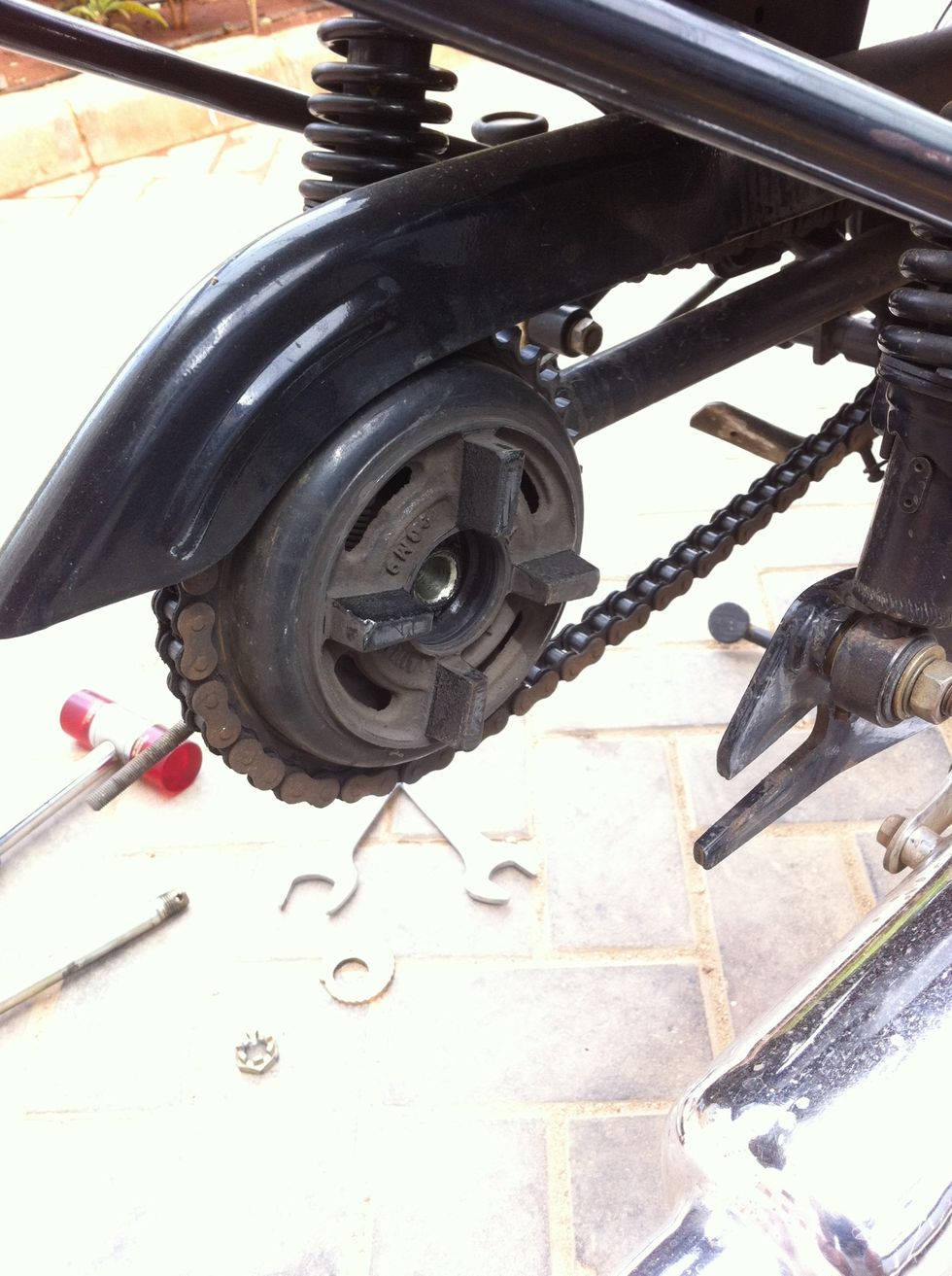 The rear wheel can be easily pulled out by tilting the bike to the left of the motorcycle. Now you see the chain and brake assembly here. You can choose not to remove the chain links.