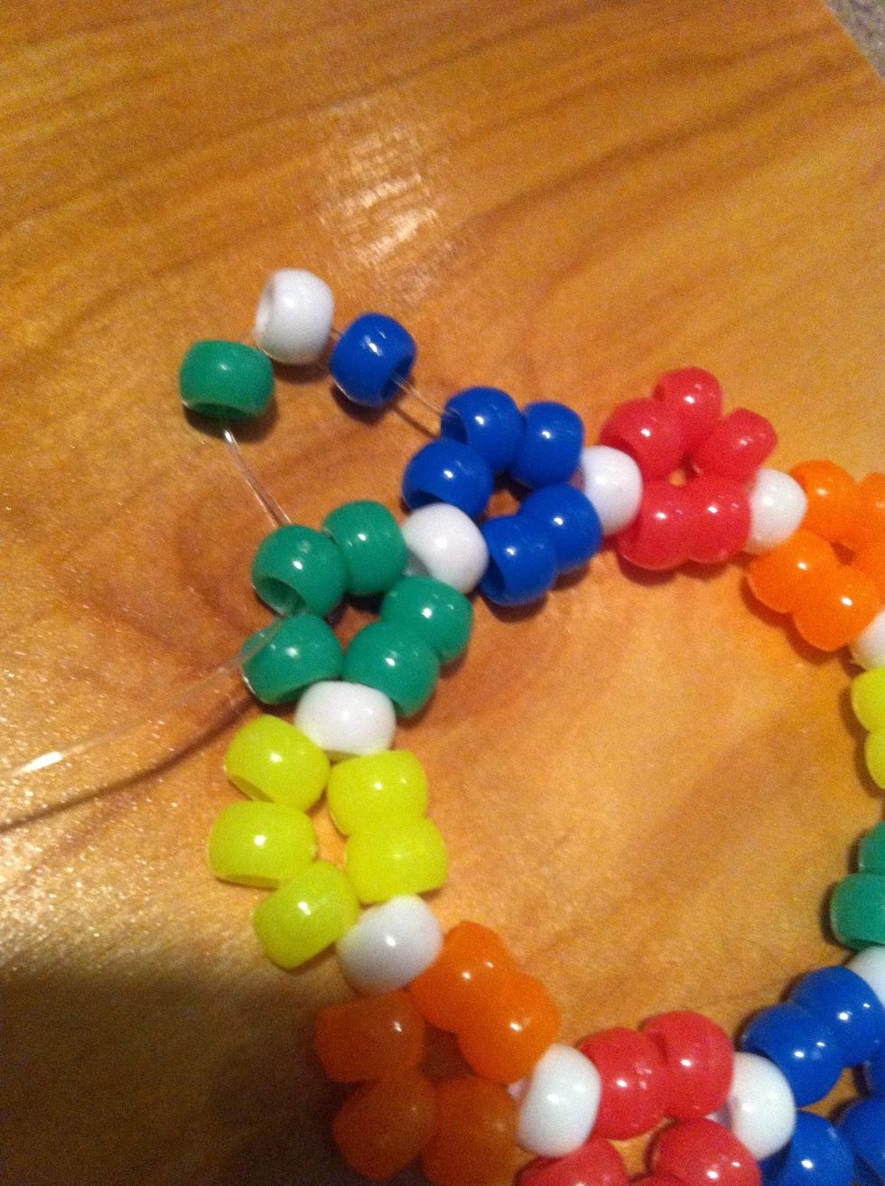 Then add in a blue, white, and green bead. After you thread that always thread a bead the same color according to the area your at, in this case you next thread a green a white and a yellow bead next.