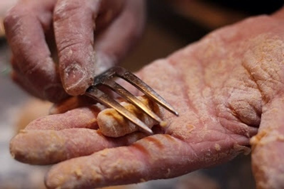 Then, divide it into about 4 portions and roll the dough into 4 long thin rolls. Cut the rolls into pieces that are about 1/2 inch long. Take the little pieces and score them on a fork...