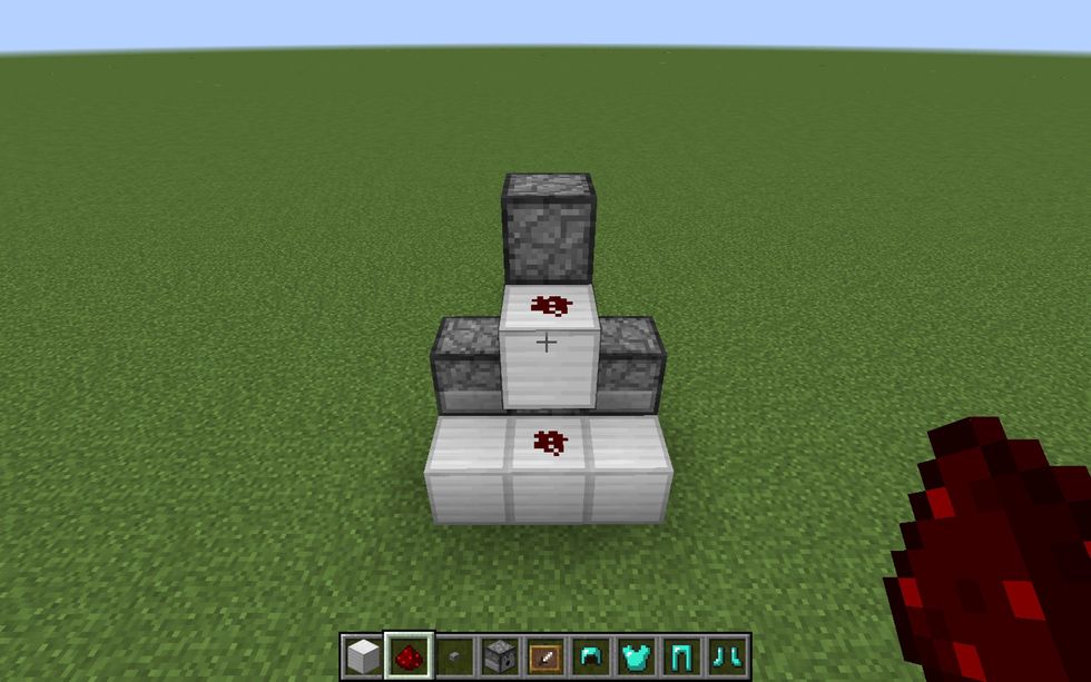 Then, go to the back and place two Redstone dust on the top and bottom middle block. This is needed to activate the dispensers on both the top and bottom.