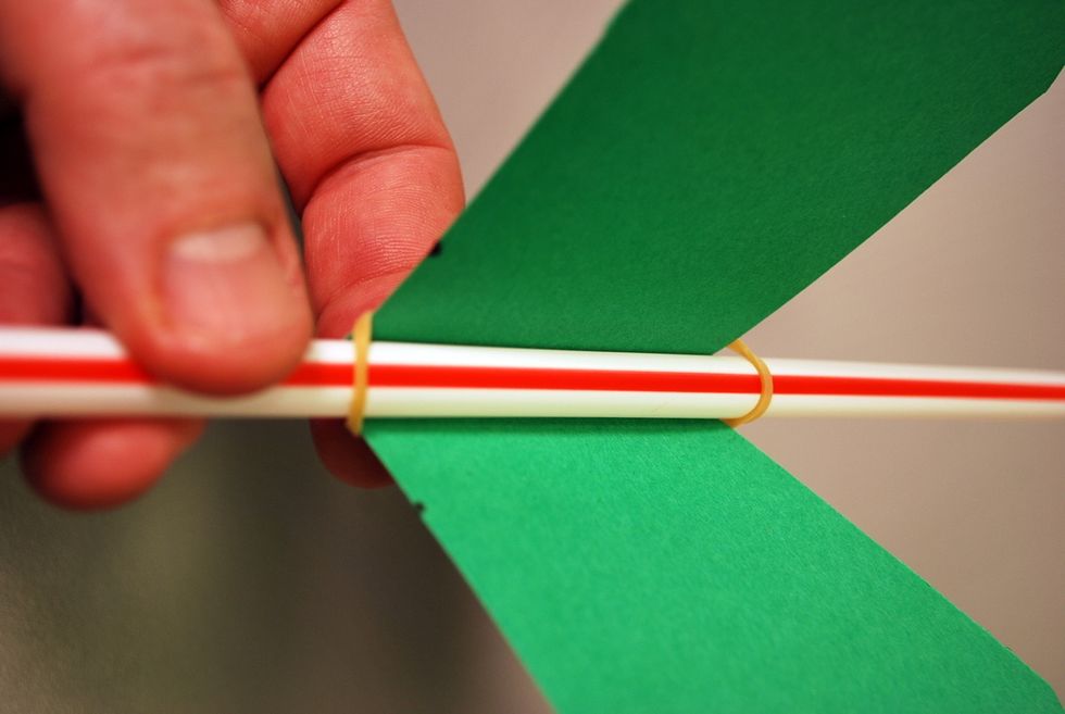 Then, stretch the rubber band over the paper fold in back and around the other end of the straw.