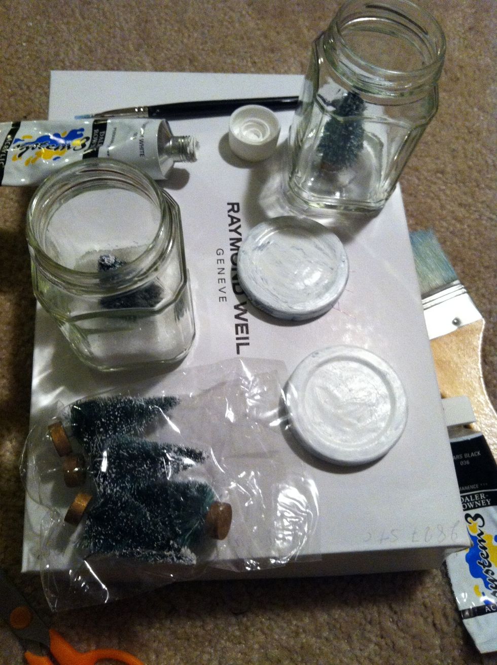 These little jars are getting trees in them. Waiting for the paint to dry on the lids. They were jelly jars & had writing on the lids, that's why they're getting painted.