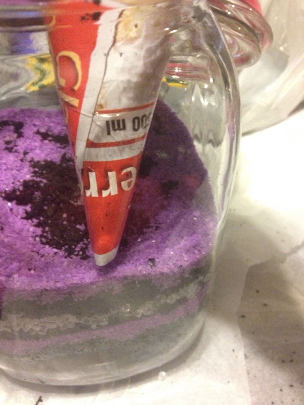 This is a photo from a different jar with purple sand. I made a funnel out of paper to direct the sand to the edges. I got the sand, glass beads and pebbles from the dollar store for about $1.25 each.