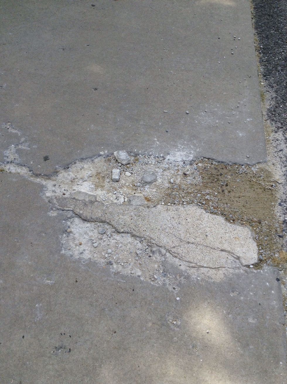 This is an example of weathering because the wind and ice wore away at the cement and created a pothole.