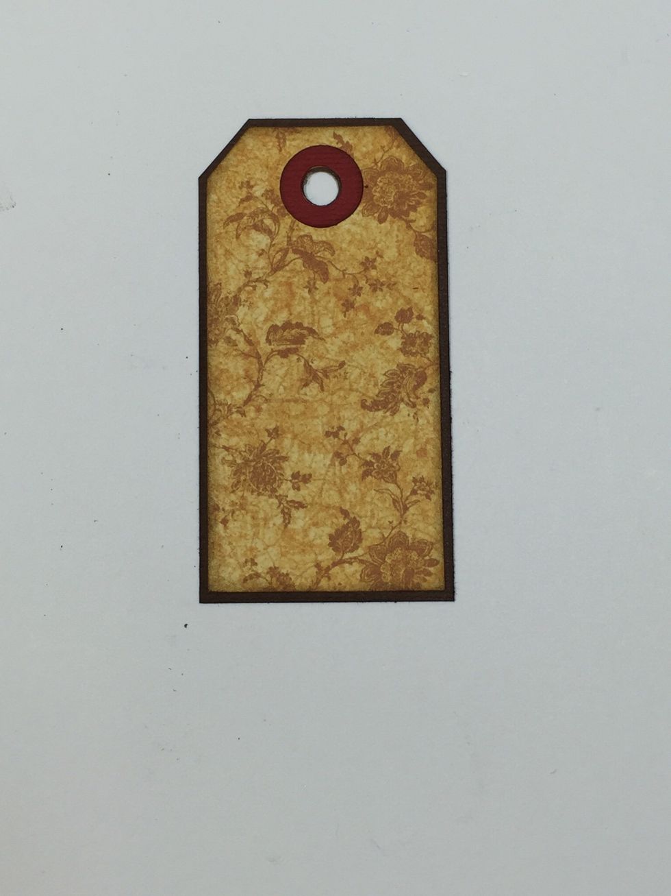 This tag was cut with Tim Holtz's "Tiny Tabs & Tags" die. Adhere to brown cardstock, slightly larger, then punch the hole and add the reinforcer circle.