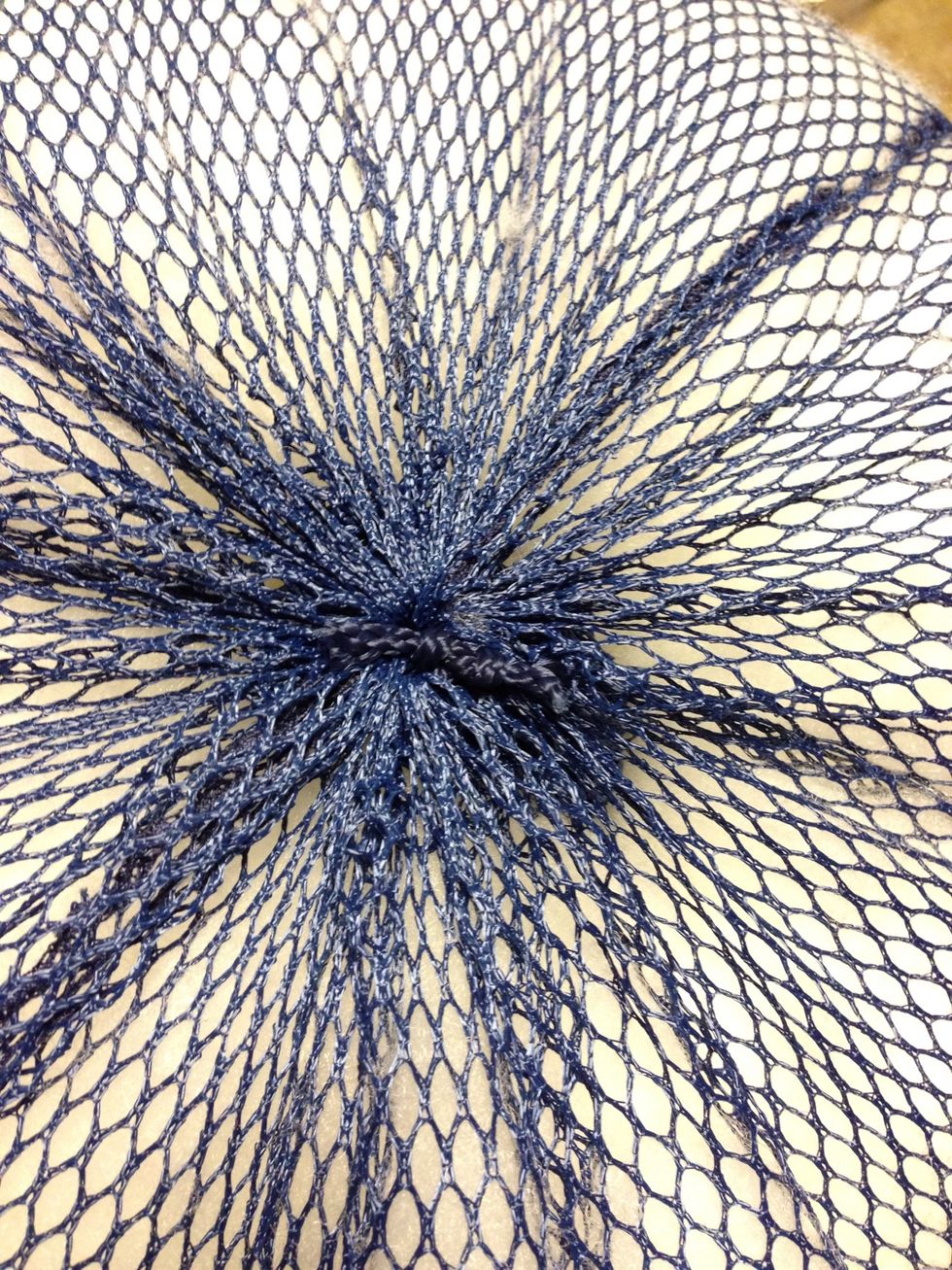 Thread that same string through the arches you see here, then open up and stuff leftover laundry bag in your hand, stuff in the hole. Then pull tight and tie a knot. Cut excess