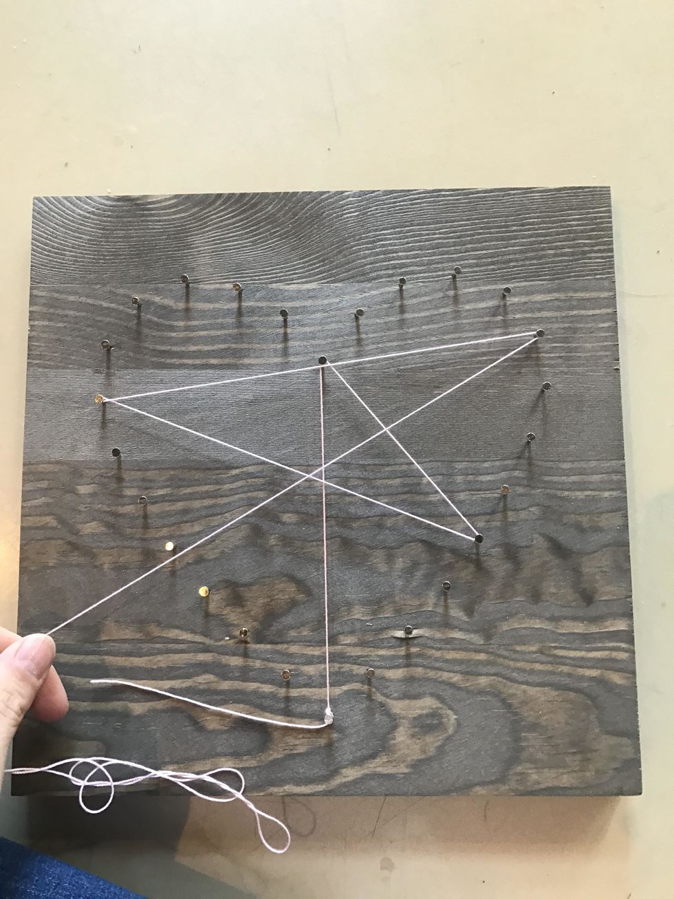 Tie a knot around any nail, as if you are tying your shoe. Double knot. Begin stringing in a random pattern so that you hit ever nail head. Occassionally, string 360 degrees around a nail so taut.