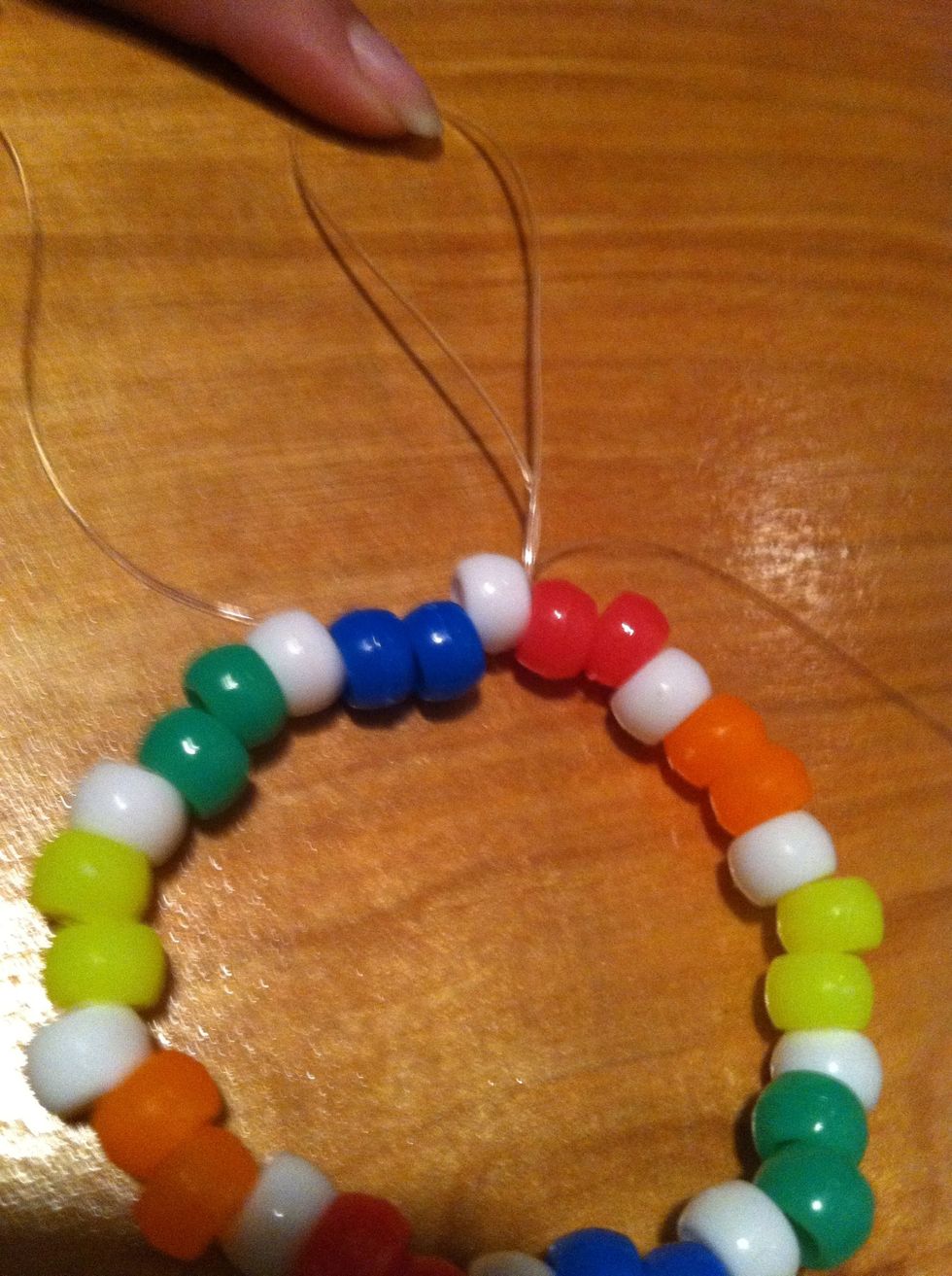 Tie the bracelet in a knot and leave some string at the end. Do not cut the shortest string. Then thread the longest string into the white bead right next to it.