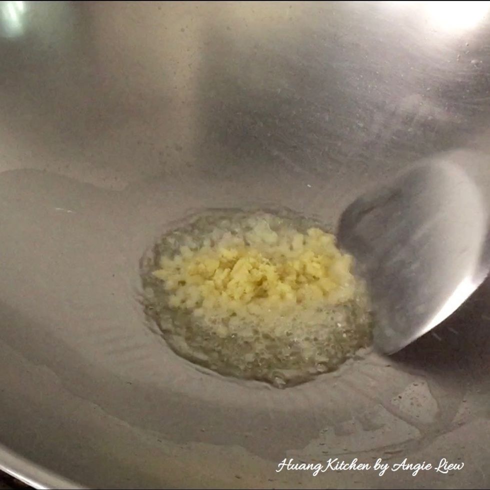 To fry the water spinach, first heat oil in a wok over high heat. Then add in minced ginger and stir fry for 10 seconds.