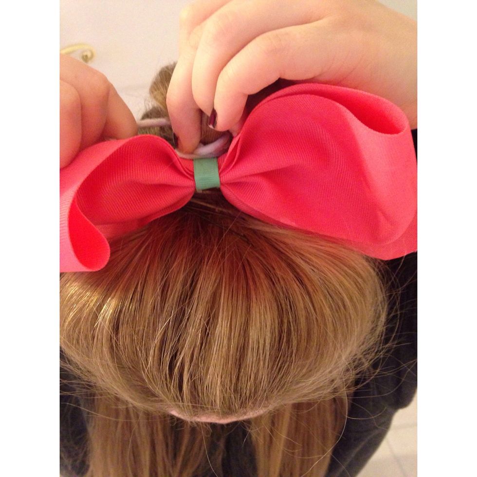 To put the bow in, place it between the poof and ponytail you have just made. Wrap the ponytail attached to the bow around the ponytail you made.