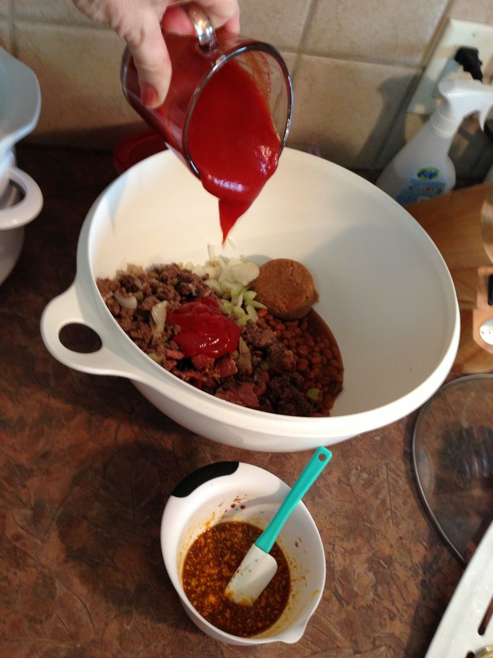 To the baked beans, add meats, brown sugar, a cup of ketchup and other smaller ingredients.