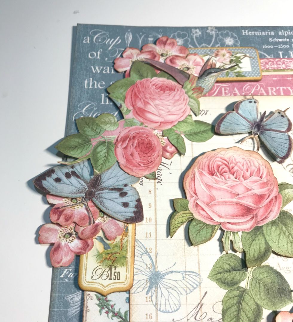 To the left of small rose, adhere the other chipboard banner, 3 pink flowers and a butterfly.