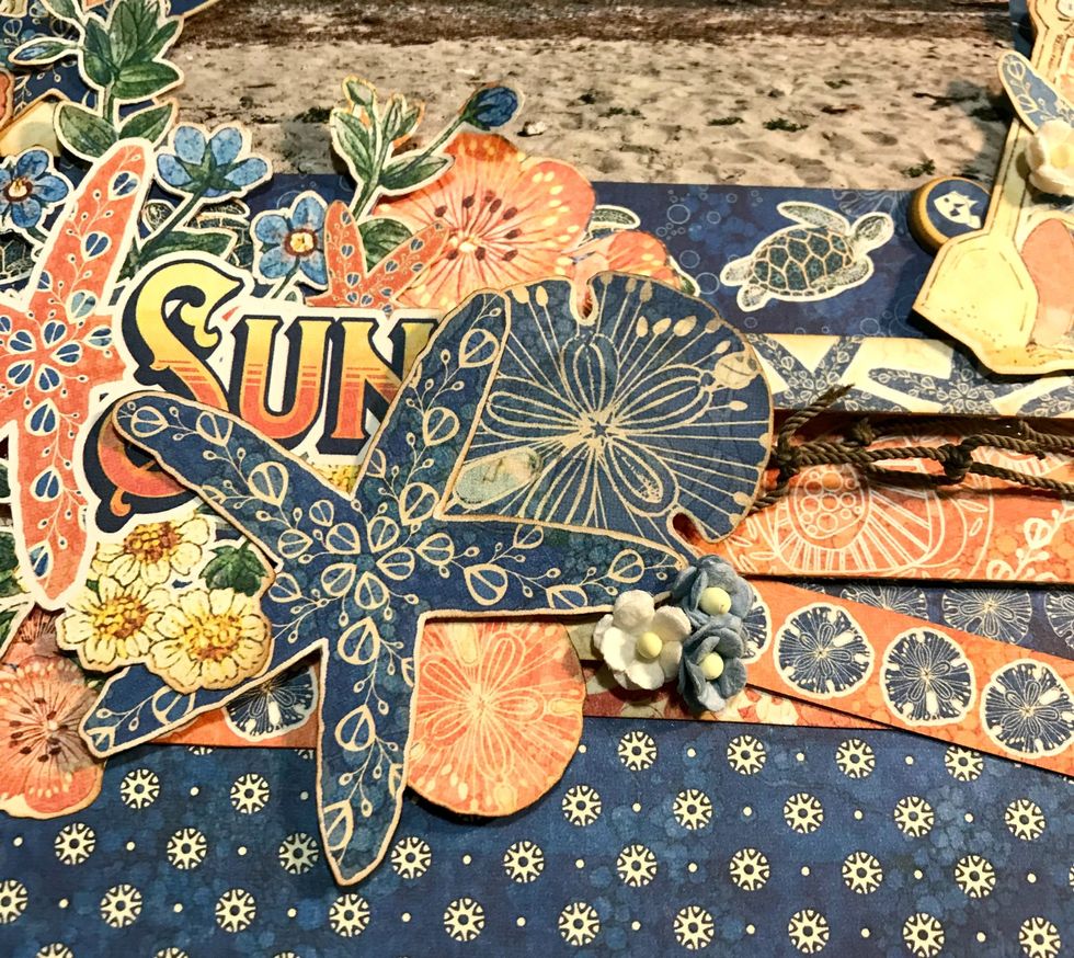 To the right of the starfish, adhere 1 pink sand dollar, 2 blue flowers and 1 whiter flowers. By the pink flower bunch, adhere 1 coral starfish.