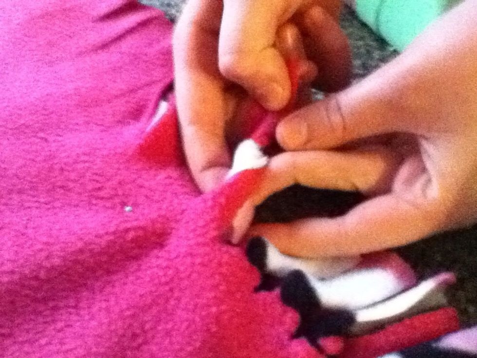 To tie the knot, take two slips of fleece and move the bottom slip over the top and through the gap. Now take the top slit over the bottom and through the gap. Tighten the knot again.