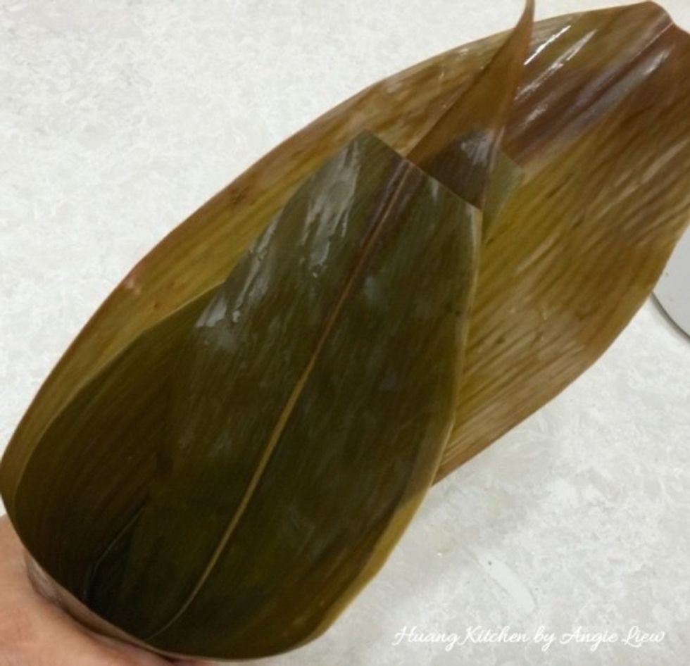 To wrap the rice dumplings, first overlap 2 bamboo leaves by about 80% of the area. Then fold from the centre to form a cone.