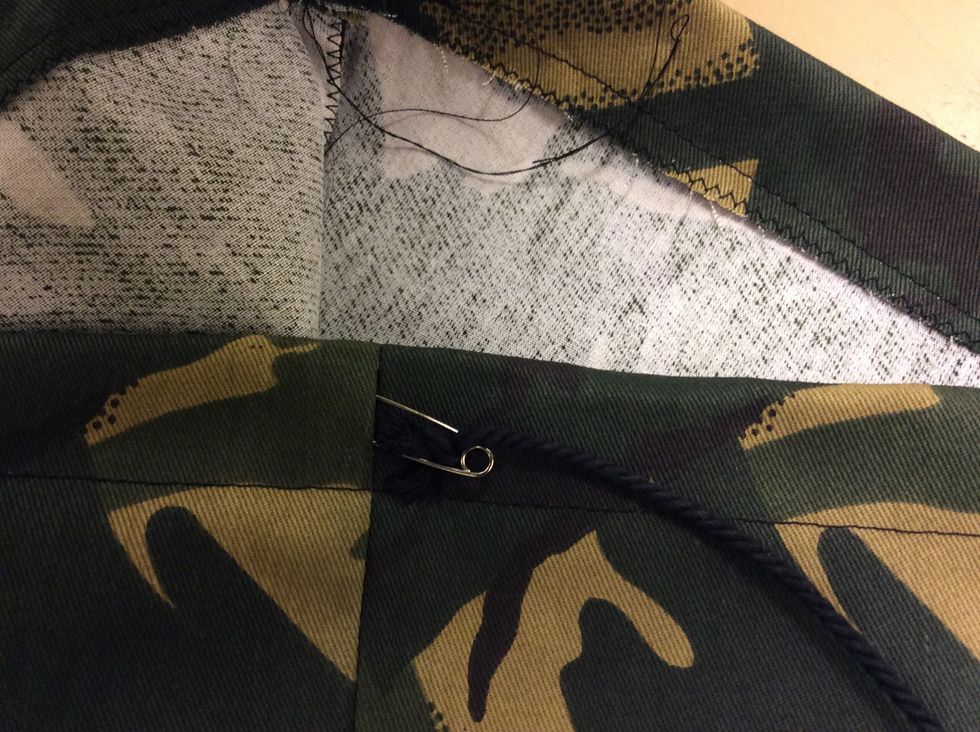 Tr\u00e4 in s\u00e4kerhetsn\u00e5len med snodden i \u00f6ppningen p\u00e5 ena sidan \u00f6verkanten. Tr\u00e4 den sedan runt hela tunneln s\u00e5 att den kommer ut igen ur samma \u00f6ppning som du tr\u00e4dde in den i.