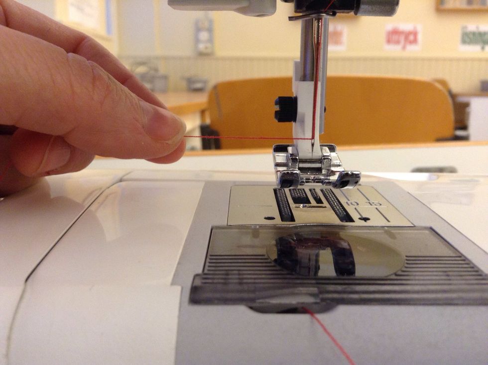 Tr\u00e4 tr\u00e5den genom n\u00e5ls\u00f6gat. Det kan g\u00e5 l\u00e4ttare om du f\u00f6rst klipper av tr\u00e5den.