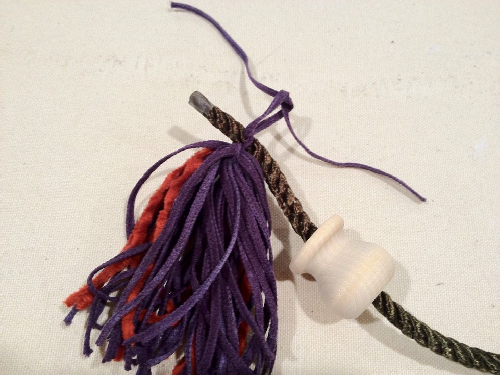 Trim off the excess tape, leaving a small amount on the end of the cording to keep it from unraveling. Tie one of your tassels tightly about 1/2" from one end of the cord.
