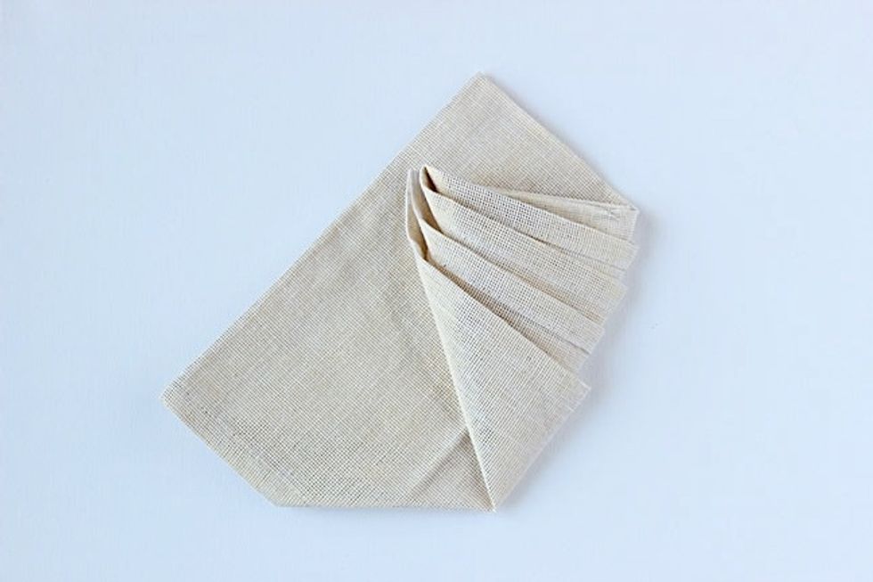 Turn the napkin over, holding all the layers you folded in place. Then, bring the right corner up and to the left side as pictured.