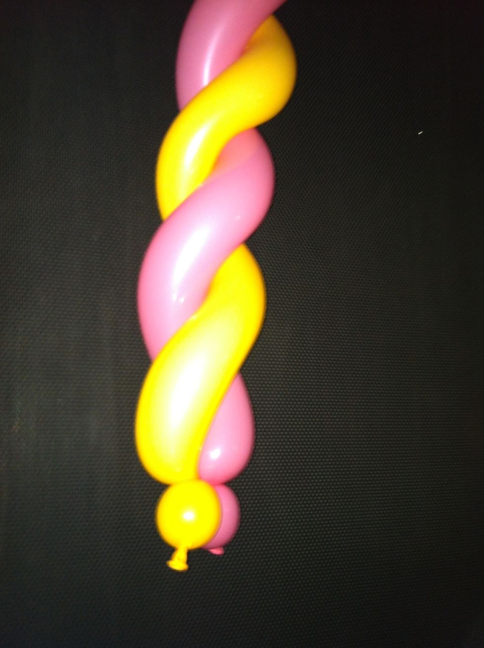 Twist the balloons together. (tip: hold bottom where the balloons are connected w knees and use hands to spiral balloons around each other...)