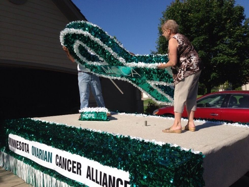 Two people should carefully climb up on the float and remove the large teal ribbon from the pegs.