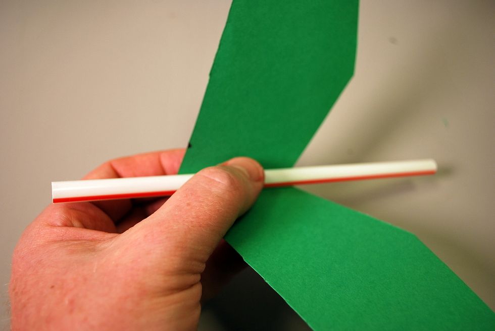 Unfold the wings then place a straw inside of the fold.