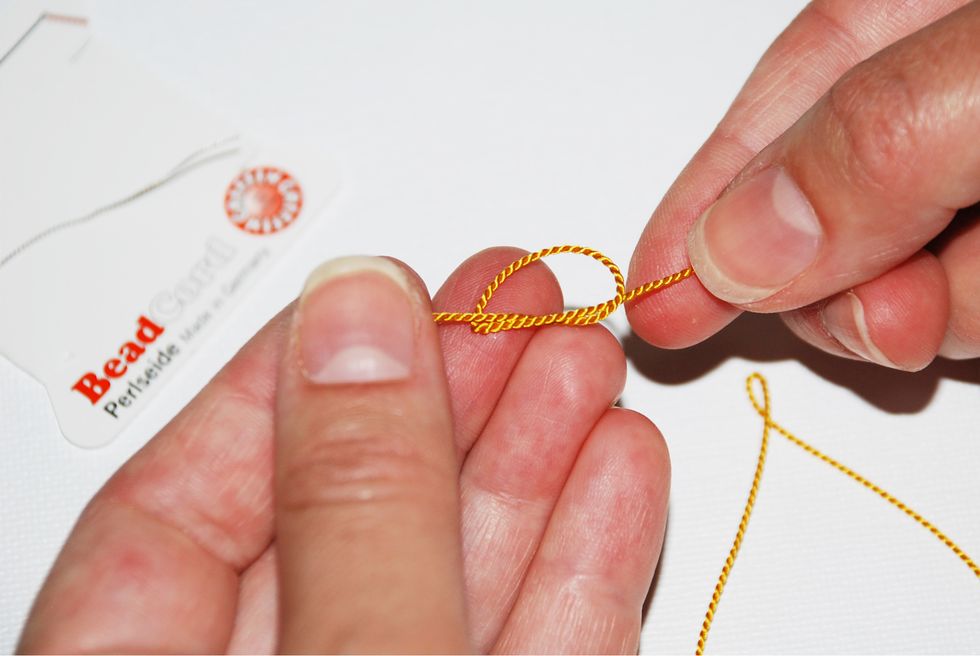 Unravel your knotting thread from the card and tie a knot all the way at the end of the 2 meter thread (opposite of the needle end).