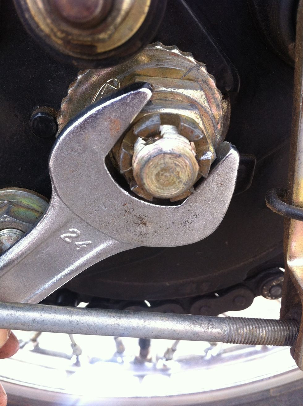 Use a 24 mm spanner to remove the first nut. Rotate anti clock wise to remove this nut. This is the nut that holds the stud that holds the entire rear wheel.