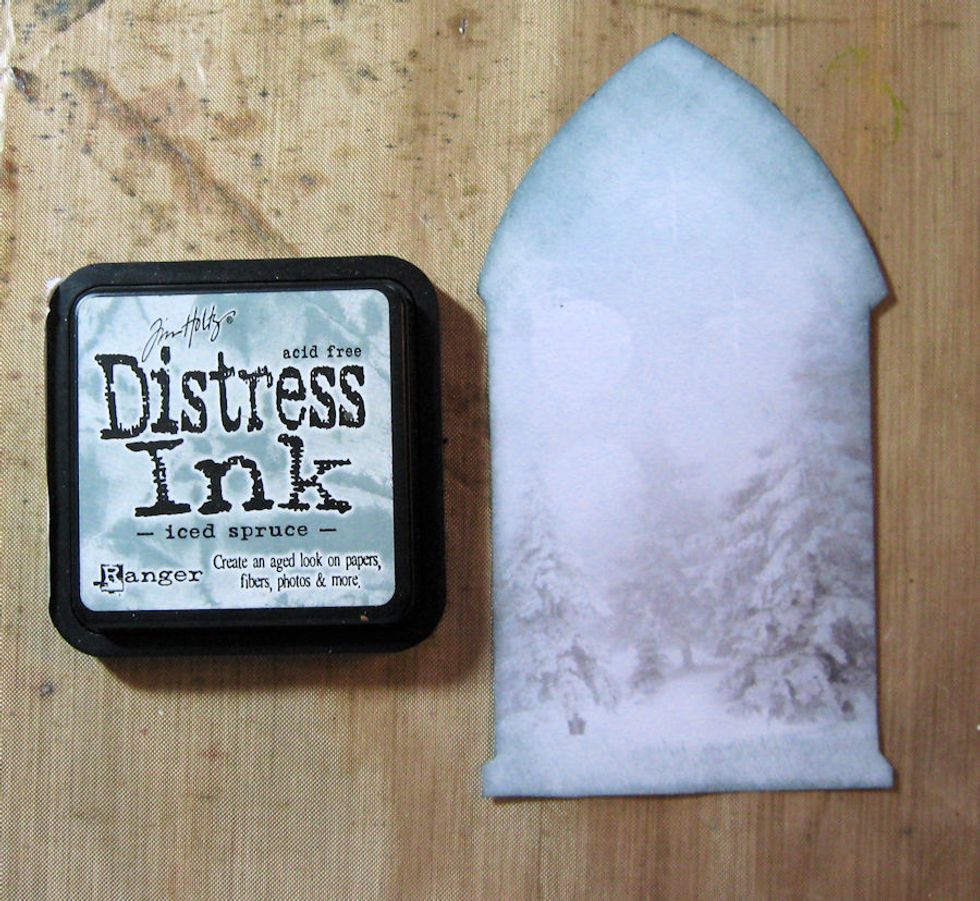 Use a blending tool to add Iced Spruce Distress Ink to the edges of the cut out paper.  Glue to the back of the frame.  Burnish with a bone folder to get rid of any air bubbles. Set aside.