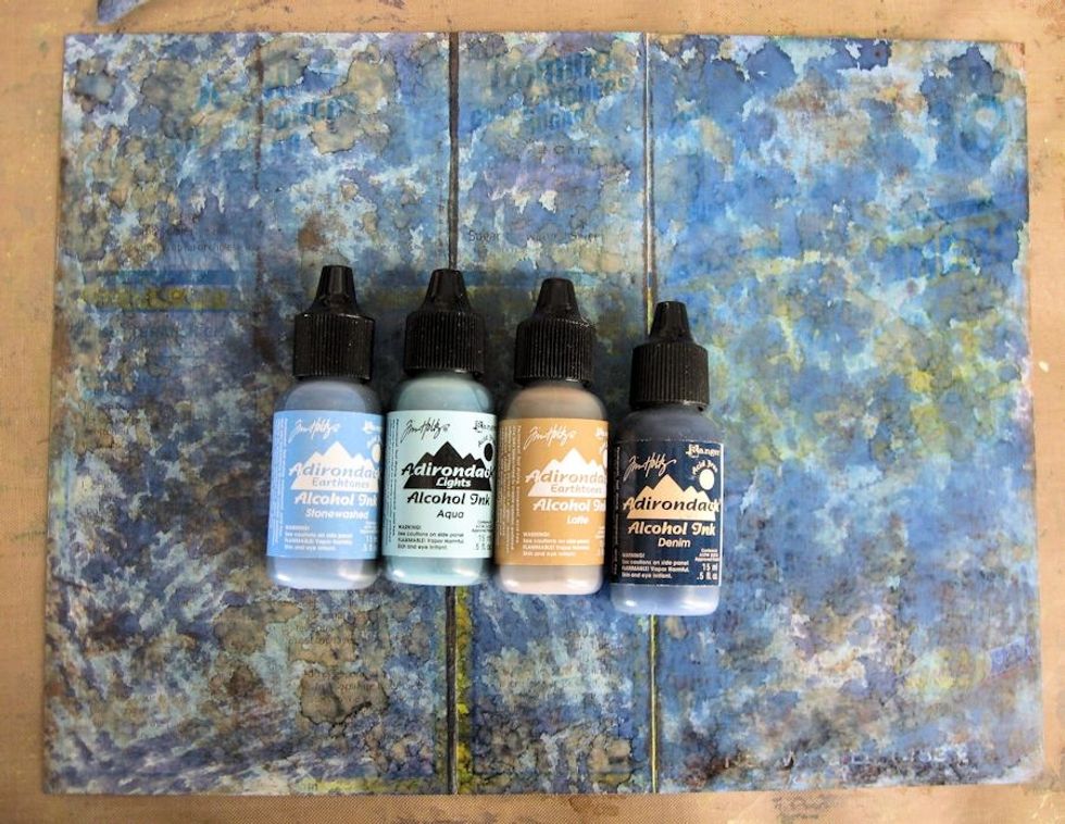 Use a felt applicator and blending tool to apply the following Ranger Alcohol ink colors to the sanded surface: Stonewashed, Aqua, Latte, and Denim. Blend with Ranger Blending Solution.