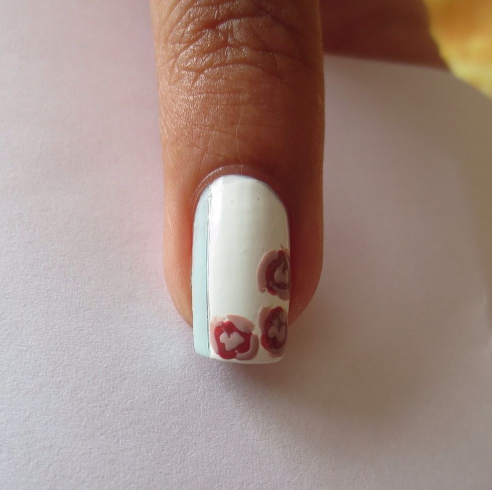 Use a fine nail art brush or toothpick and use a lighter pink polish to add small strokes randomly around the dark red circles to make petals
