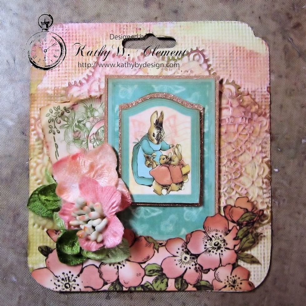 Use a hot glue gun to attach a hydrangea blossom. Glue the Botanica Mini on top, as shown. This anchors the corner. Continue to layer in flowers and leaves around the focal image.