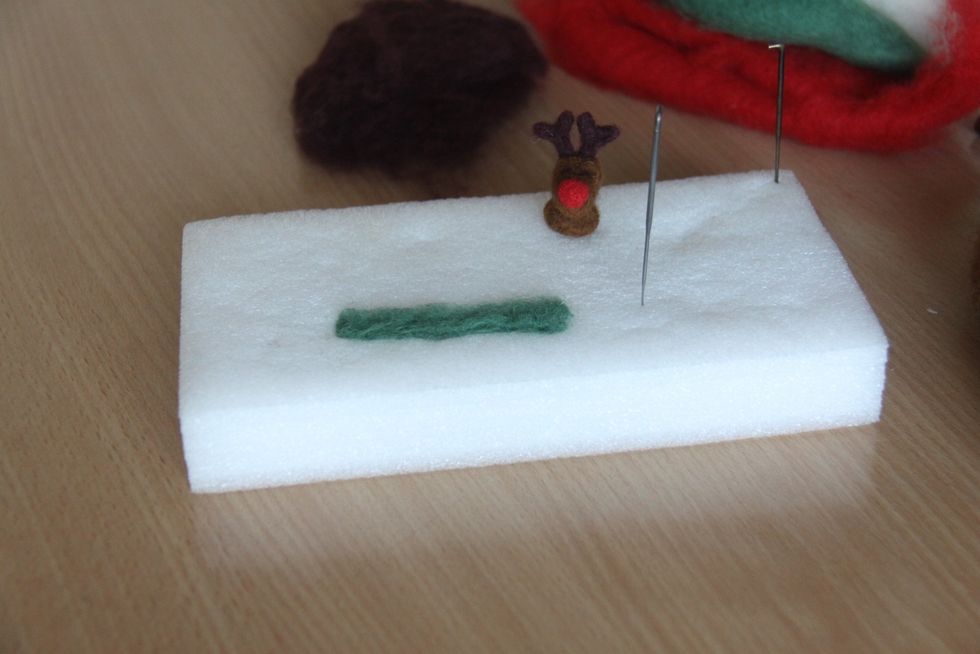 Use a little bit of green wool, spread on the pad to make the shape of a scarf. Punch shallowly onto the place that you lay your wool. Turn to the other side and punch until you make a smooth scarf.