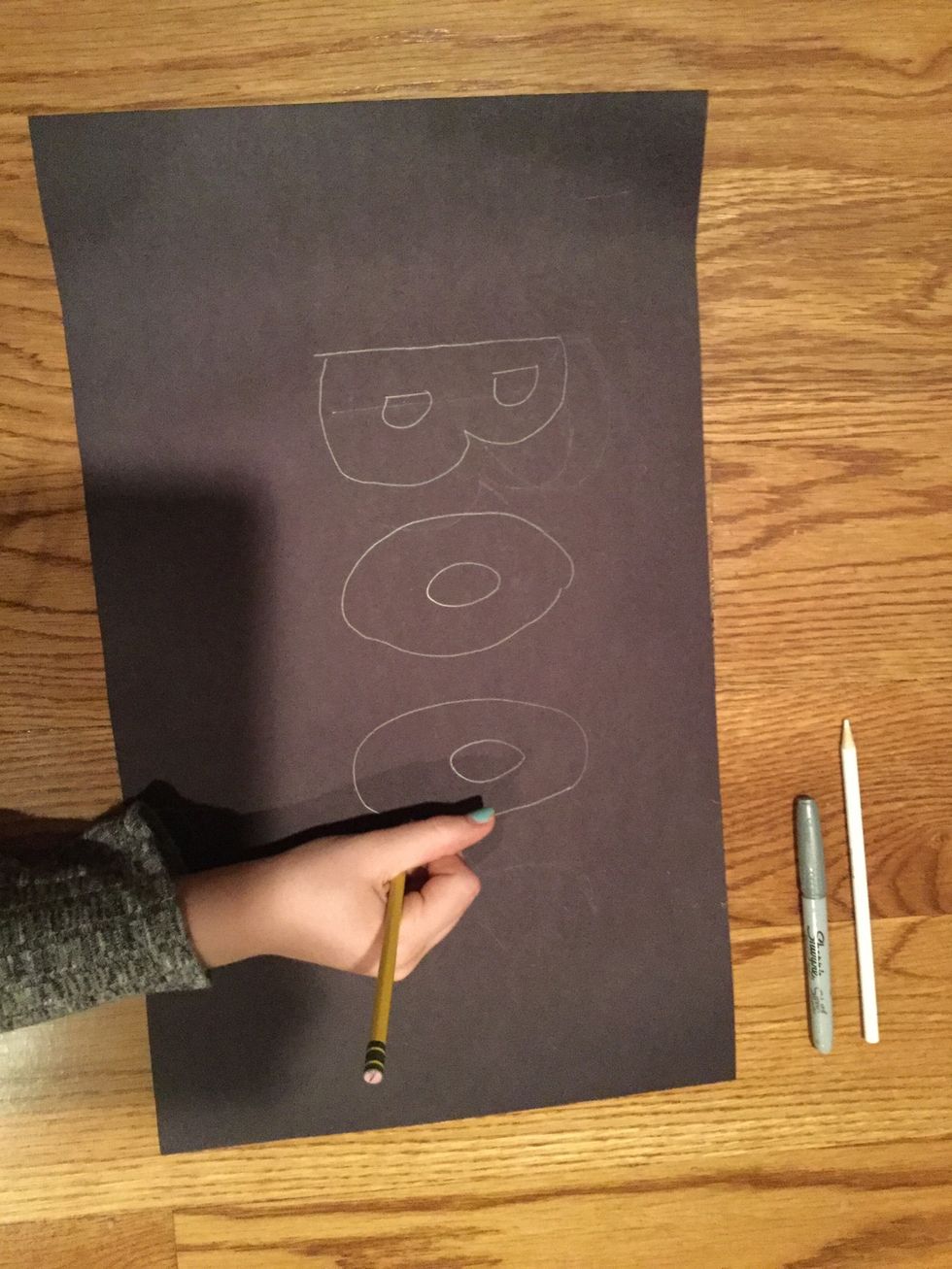 Use a pencil to write the desired Halloween word on black construction paper.