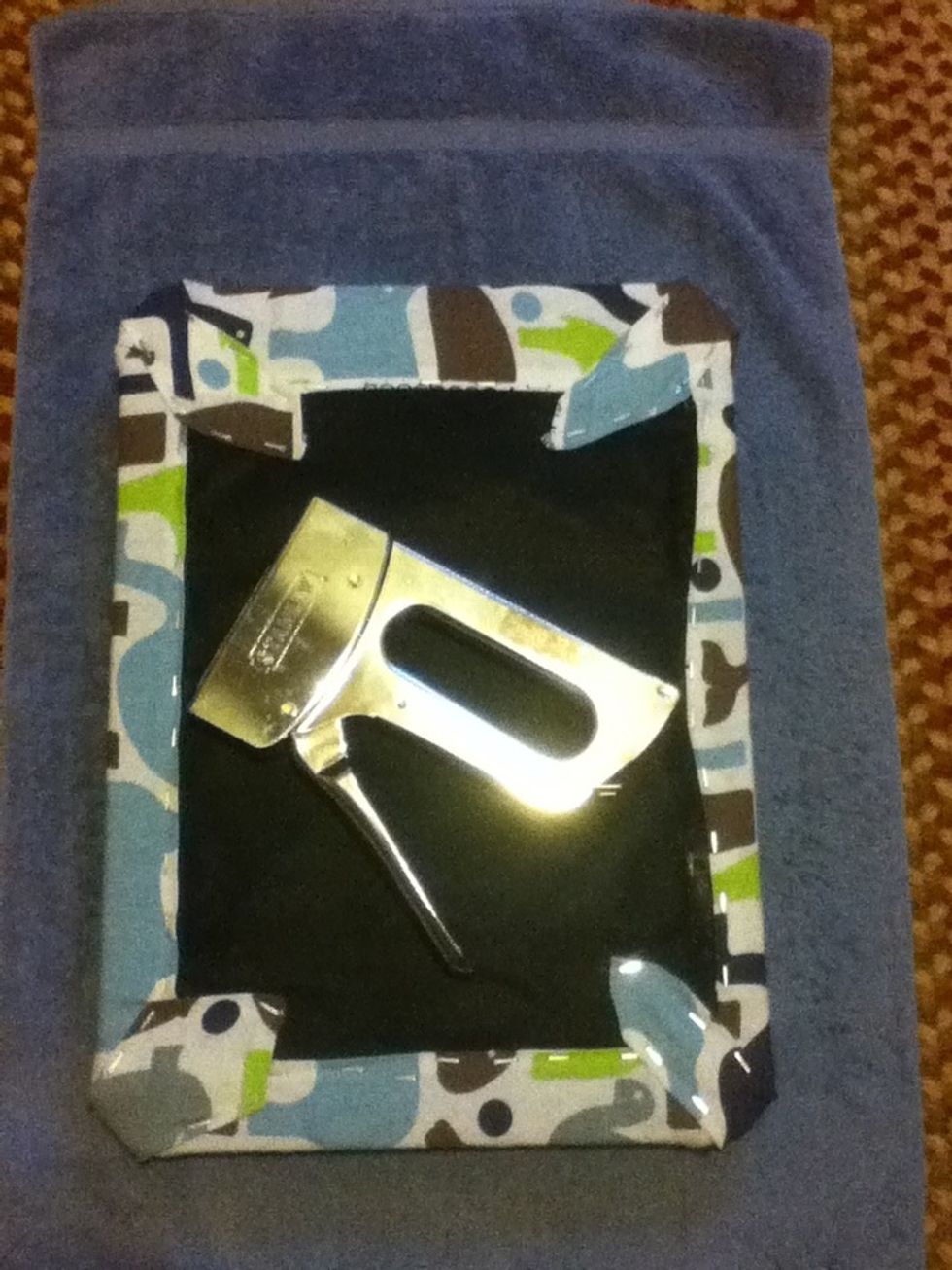 Use a staple gun to secure the fabric around the bottom of the stool lid. Start with the marked center then move outward. Tuck and pleat the corners. Be sure to pull the fabric snug before stapling.