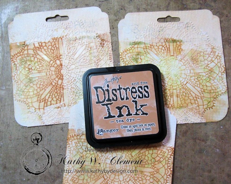 Use foam applicator to sponge Tea Dye Distress ink over the embossed edges of the tag. You may have to sand very lightly if there is gesso on the tag, as it will resist the ink. Sand lightly & ink.