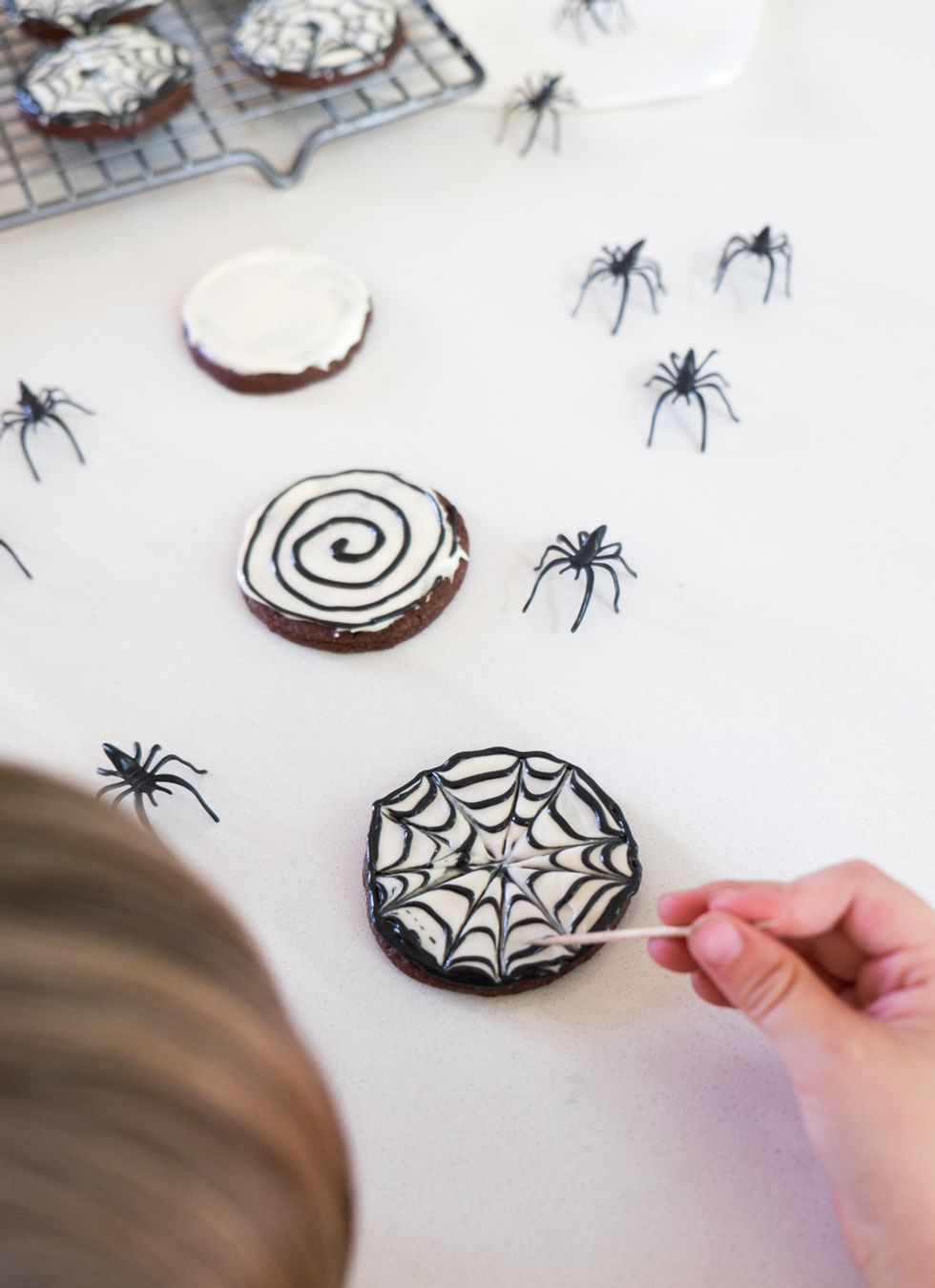 Use knife to frost cookies with white frosting, then pipe black frosting in a circle pattern on the cookie. Draw toothpick from center of the cookie out to the edge at irregular intervals.