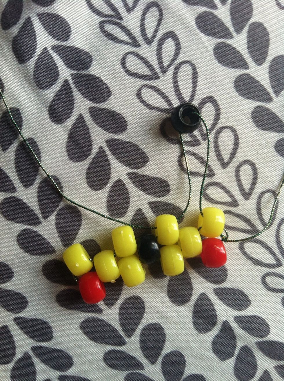 Use one string, thread it through the yellow and add a black bead, then thread it through the yellow bead sticking out.